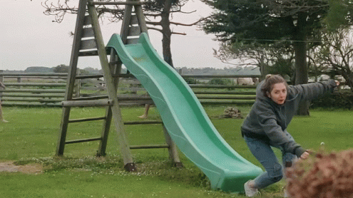 A Girl Is Playing On A Green Slide In A Grassy Field GIF