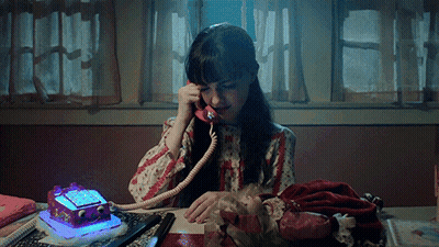 A Girl Is Sitting At A Desk Talking On A Telephone GIF