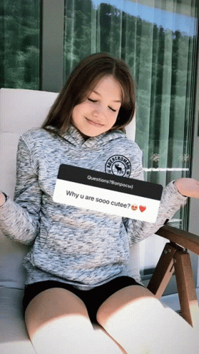 A Girl Is Sitting In A Chair Holding A Question About Why She Is Sooo Cute GIF