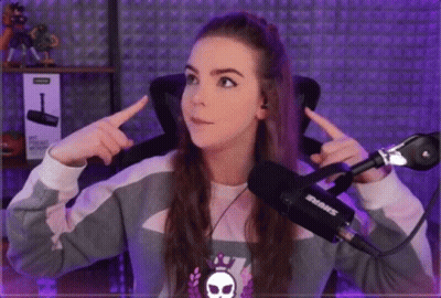 A Girl Is Sitting In Front Of A Shure Microphone And Pointing At Herself . GIF