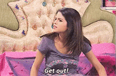 A Girl Is Sitting On A Bed With The Words Get Out Written On Her Shirt GIF