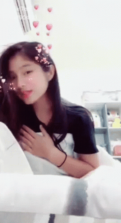 A Girl Is Sitting On A Chair With Her Hands On Her Chest GIF