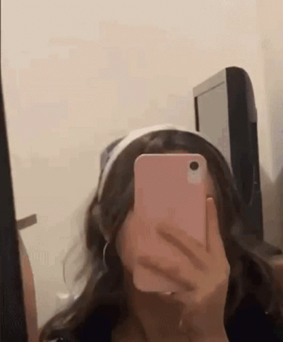 A Girl Is Taking A Selfie In Front Of A Mirror With Her Cell Phone . GIF