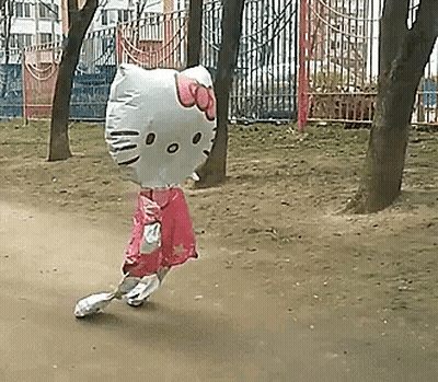 A Girl Is Walking With A Hello Kitty Balloon On Her Head In A Park . GIF
