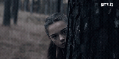 A Girl Peeking Out From Behind A Tree With The Netflix Logo In The Background GIF