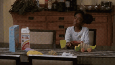 A Girl Sits At A Table With A Box Of Milk And Cereal GIF