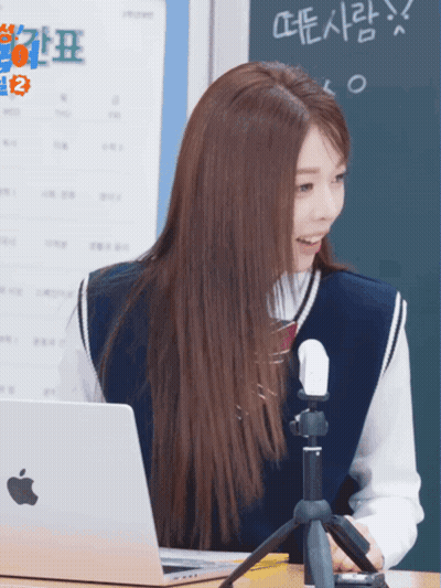 A Girl Sitting At A Desk With An Apple Laptop And A Microphone GIF