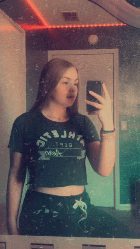 A Girl Taking A Picture Of Herself In A Mirror Wearing A Crop Top That Says Jht GIF