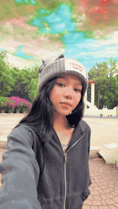 A Girl Wearing A Beanie And A Jacket Taking A Selfie GIF