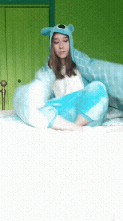 A Girl Wearing A Blue Hat And A Blue Blanket Is Sitting On A Bed GIF
