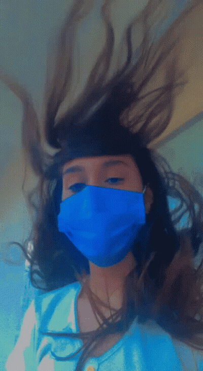 A Girl Wearing A Blue Mask Has Her Hair Blowing In The Wind GIF