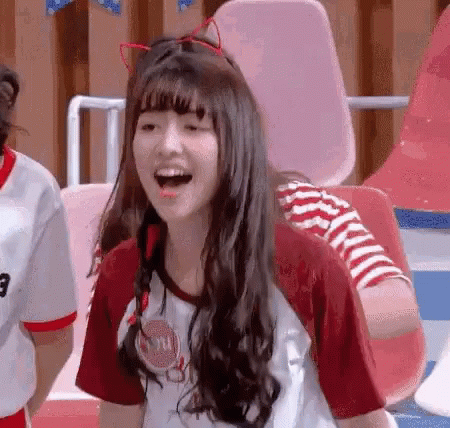 A Girl Wearing A Cat Ear Headband And A Red Shirt Is Laughing With Her Mouth Open . GIF