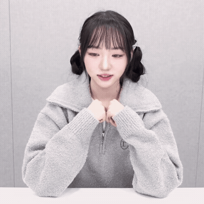 A Girl Wearing A Grey Sweater With The Letter T Embroidered On It GIF