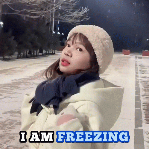 A Girl Wearing A Hat And Scarf Is Standing In The Snow With The Words I Am Freezing Below Her GIF