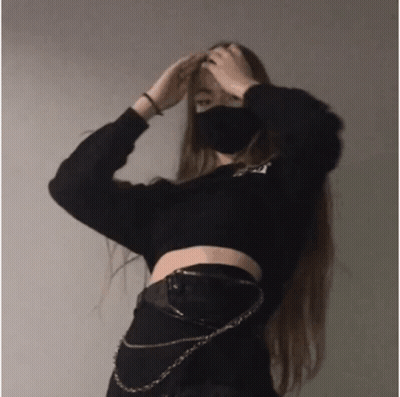 A Girl Wearing A Mask And A Black Crop Top Is Standing In Front Of A Wall . GIF