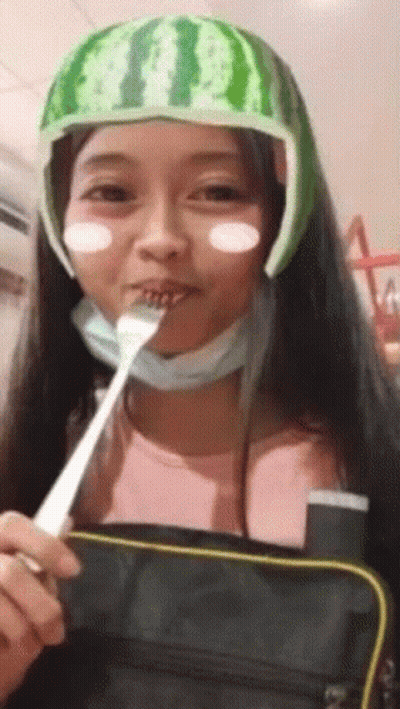 A Girl Wearing A Watermelon Hat Is Eating With A Fork . GIF