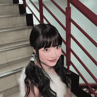 A Girl Wearing A White Fur Vest And Earrings With The Letter N On Them GIF