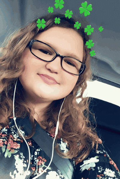 A Girl Wearing Glasses And A Floral Shirt Has Green Clovers On Her Head GIF