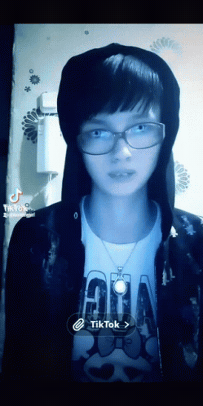 A Girl Wearing Glasses And A Hoodie Has A Tiktok Icon On The Bottom Right GIF