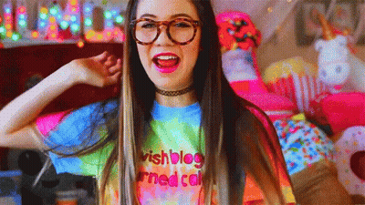 A Girl Wearing Glasses And A Tie Dye Shirt With The Words Wishblog Written On It GIF