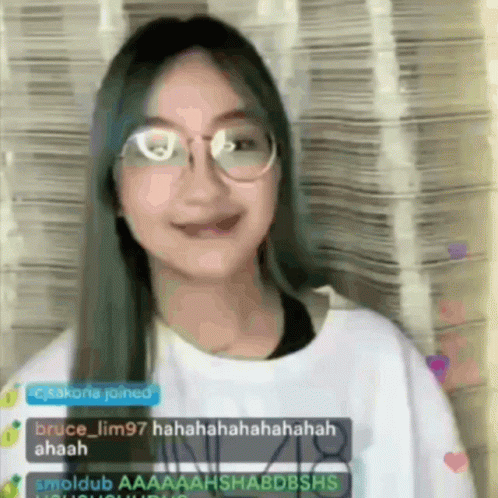 A Girl Wearing Glasses And A White Shirt Is Smiling And Laughing While Talking To Someone On A Live Stream . GIF