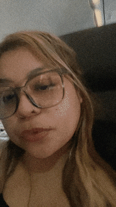A Girl Wearing Glasses Looks At The Camera With A Blurry Background GIF