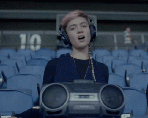 A Girl Wearing Headphones And Holding A Boombox In Front Of A Stadium With The Number 10 On The Wall GIF