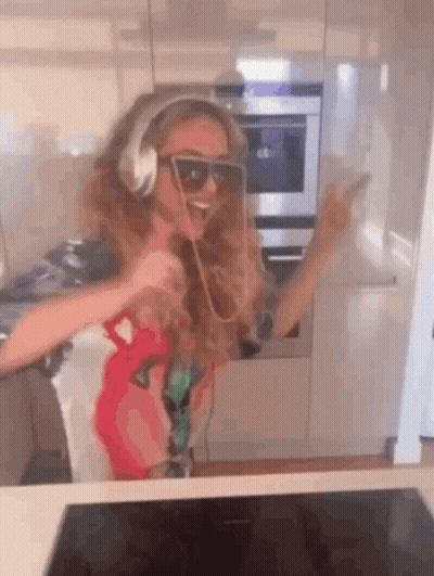 A Girl Wearing Headphones And Sunglasses Is Dancing In The Kitchen . GIF
