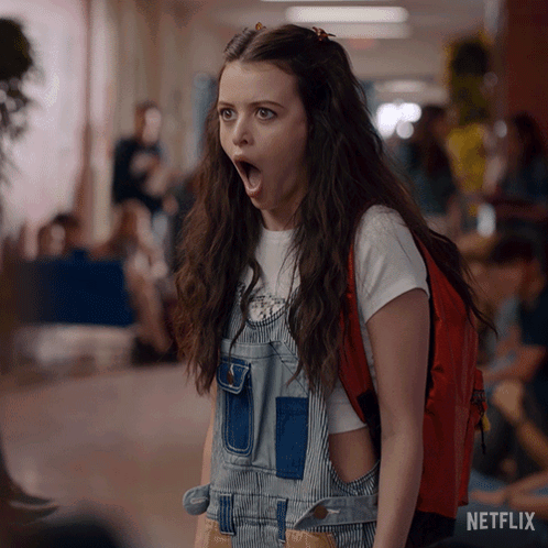 A Girl Wearing Overalls And A Red Backpack With A Netflix Logo On The Bottom GIF