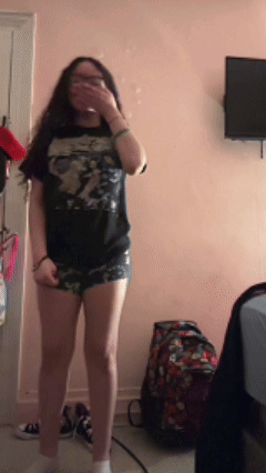 A Girl Wearing Shorts And A Black Shirt Is Standing In A Room GIF