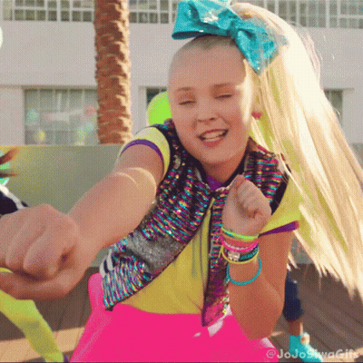 A Girl With A Blue Bow In Her Hair Is Pointing At The Camera GIF