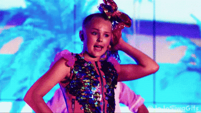 A Girl With A Bow In Her Hair Is Standing In Front Of A Blue Wall . GIF