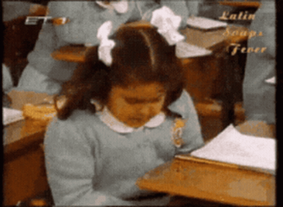 A Girl With A Bow In Her Hair Sits At A Desk In A Classroom With Latin Soups Fever Written On The Bottom GIF