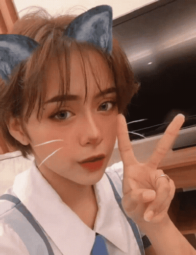 A Girl With A Cat Ear On Her Head Giving A Peace Sign GIF