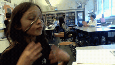 A Girl With A Chain Around Her Face Is In A Classroom With Other Students GIF