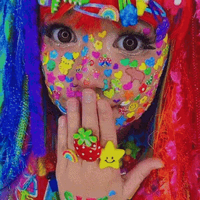 A Girl With A Lot Of Colorful Stickers On Her Face Is Wearing A Strawberry Ring And A Star Ring . GIF