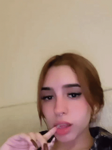 A Girl With A Piercing In Her Nose Is Making A Funny Face With Her Fingers . GIF