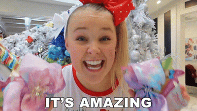 A Girl With A Red Bow On Her Head Says It 'S Amazing In Front Of A Christmas Tree GIF