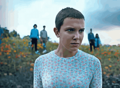 A Girl With A Very Short Haircut Is Standing In A Field Of Flowers GIF