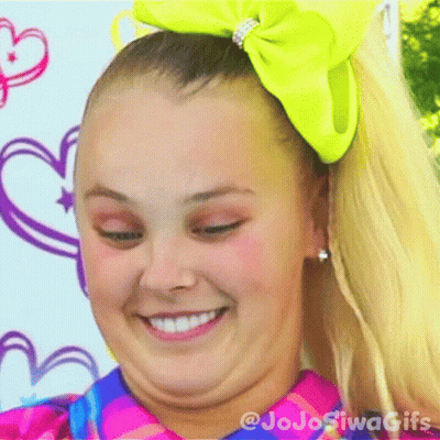 A Girl With A Yellow Bow In Her Hair Is Smiling And Making A Face . GIF