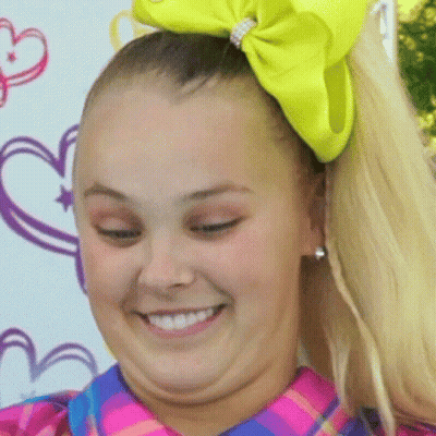 A Girl With A Yellow Bow In Her Hair Smiles For The Camera GIF