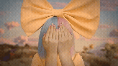 A Girl With A Yellow Bow On Her Head Covers Her Face With Her Hands GIF