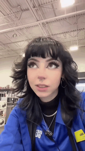 A Girl With Black Hair And A Nose Ring Is Wearing A Blue Jacket And Earrings . GIF