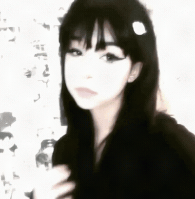 A Girl With Black Hair And Bangs Is Wearing A Black Hoodie And A Flower In Her Hair . GIF