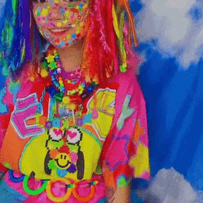 A Girl With Colorful Hair And Face Paint Is Wearing A Colorful Shirt And Necklaces . GIF