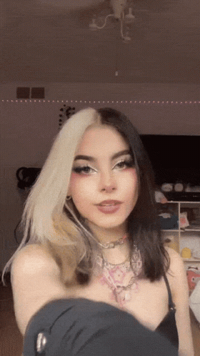 A Girl With Half White And Half Black Hair Is Taking A Selfie In A Room . GIF