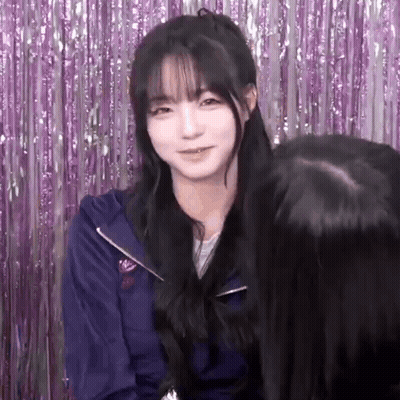 A Girl With Long Black Hair And Bangs Is Standing In Front Of A Purple Curtain . GIF