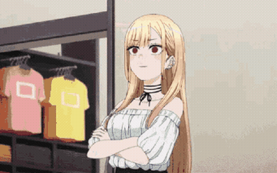 A Girl With Long Blonde Hair Is Standing With Her Arms Crossed In Front Of A Clothes Rack . GIF