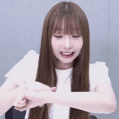 A Girl With Long Brown Hair And Bangs Is Smiling And Holding Her Hand To Her Face GIF