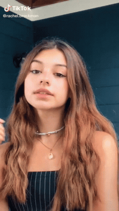 A Girl With Long Brown Hair Is Wearing A Striped Top And A Necklace GIF
